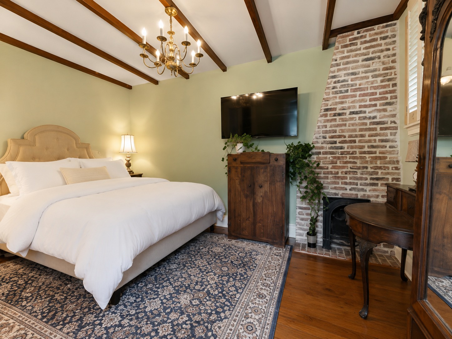 Bedroom one on level two with exposed brick fireplace, chandelier, reclaimed cypress ceiling and plush white hotel-style duvet